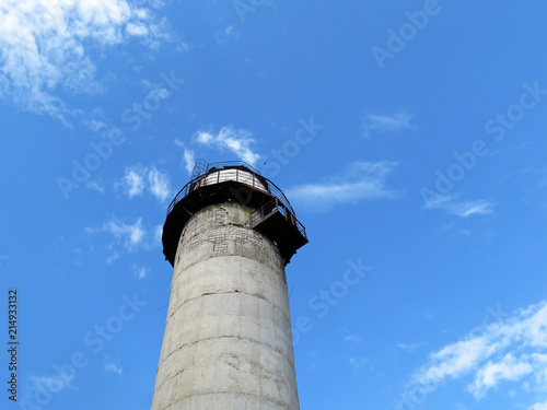 Old lighthouse tower against blue sky and white clouds, view from below