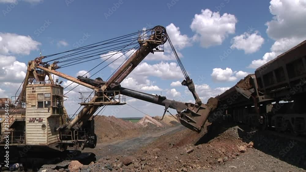 The excavator helps to unload the fossil from the railway car in the quarry. Ukraine, Krivoy Rog-25 07 2018 The excavator helps to unload the fossil from the railway car in the quarry. Ukraine, Krivoy Rog-25 07 2018