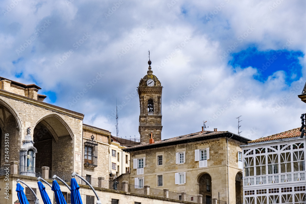 Bell tower with clock of the church of San Miguel Arcangel and typical houses of the north of Spain located in the Plaza de la Virgen Blanca in Vitoria Spain