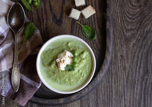 Green pea soup in bowls with spinach and cream on wooden rustic cutting board.