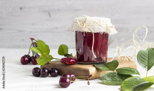 Cherry jam with fresh cherries on a wooden cutting board.