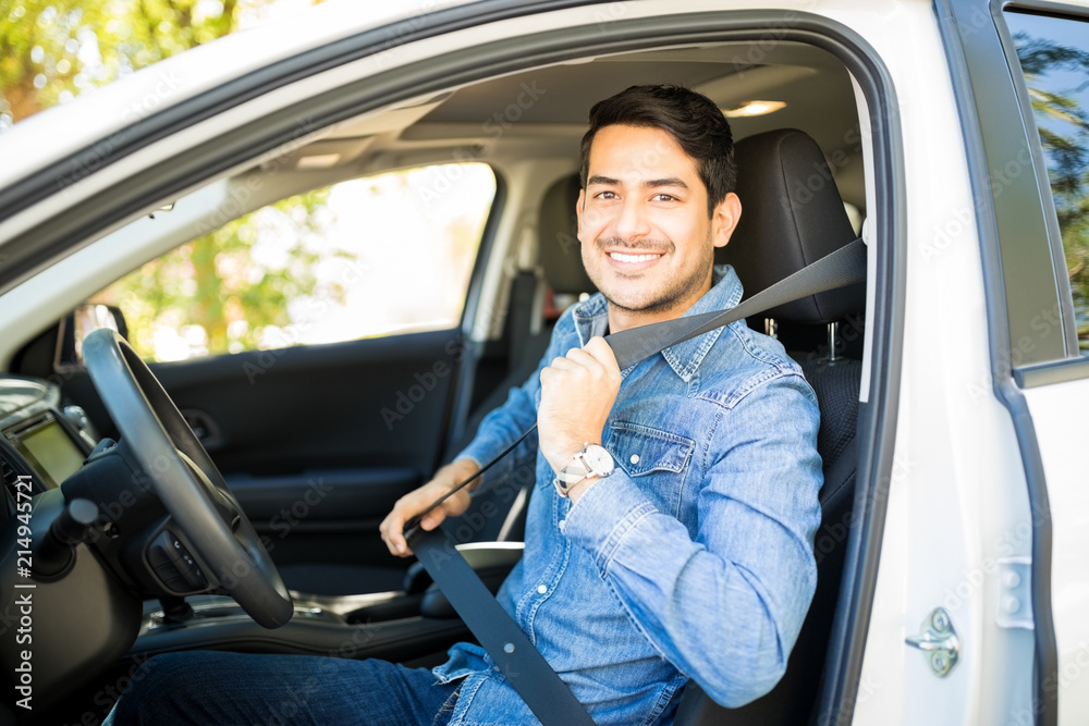 Smiling man fastening safety belt in the car