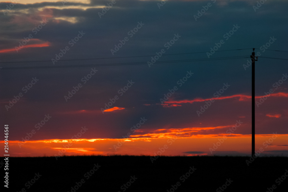 A bright orange sunset against the background of fields with grains