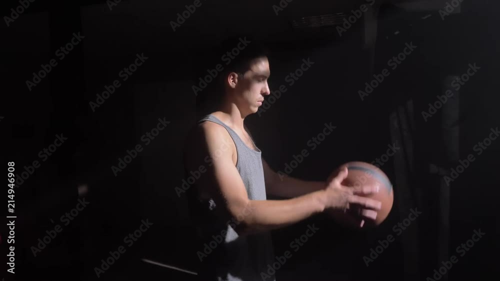 Basketball player standing in dark room and waiting, playing with ball Basketball player standing in dark room and waiting, playing with ball