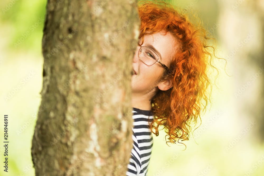 Young beautiful ginger woman hiding behind a tree outdoors Young beautiful ginger woman hiding behind a tree outdoors