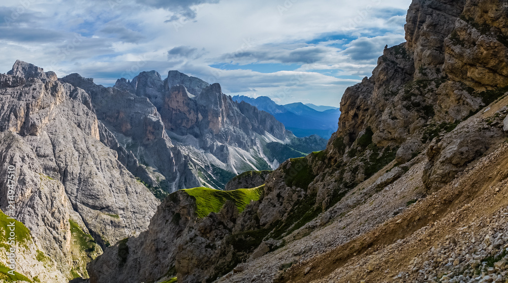 Landscape of Dolomites with green meadows, blue sky, white clouds and rocky mountains.  Italian Dolomites landscape.  Beauty of nature concept background.  The valley below.  Evening panoramic view.  