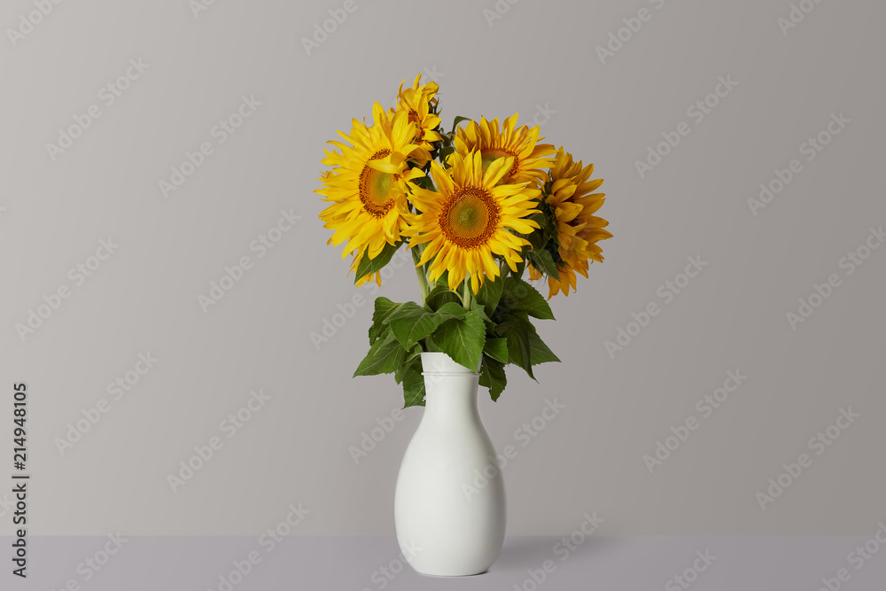 bouquet of yellow sunflowers in white vase, on grey bouquet of yellow sunflowers in white vase, on grey