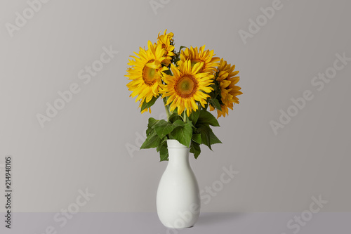 bouquet of yellow sunflowers in white vase, on grey
