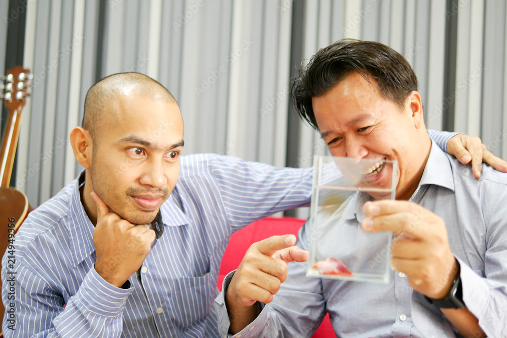 Two asian guys are seeing betta fish in the glass and very happy Two asian guys are seeing betta fish in the glass and very happy