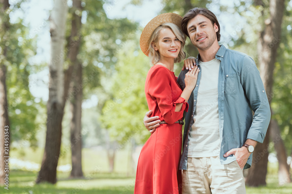 smiling girlfriend and boyfriend hugging in park and looking at camera smiling girlfriend and boyfriend hugging in park and looking at camera