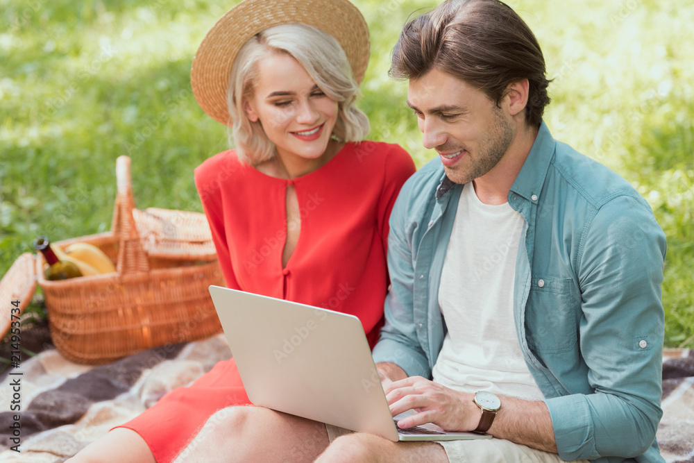 couple using laptop on blanket in park couple using laptop on blanket in park