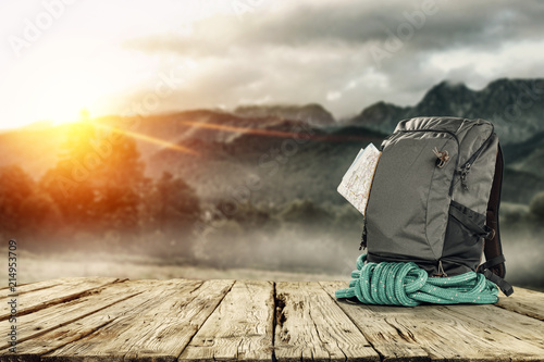 Backpack on wooden desk with free space for your decoration and mountains landscape with morning sun light 