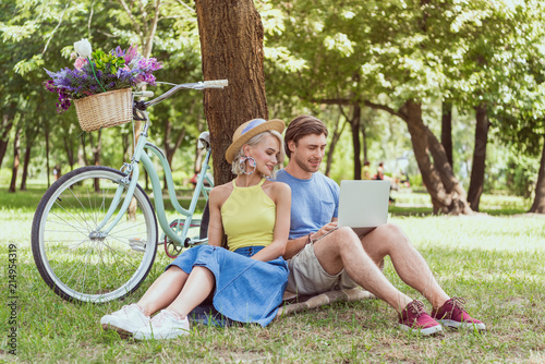 couple sitting near tree in park and using laptop
