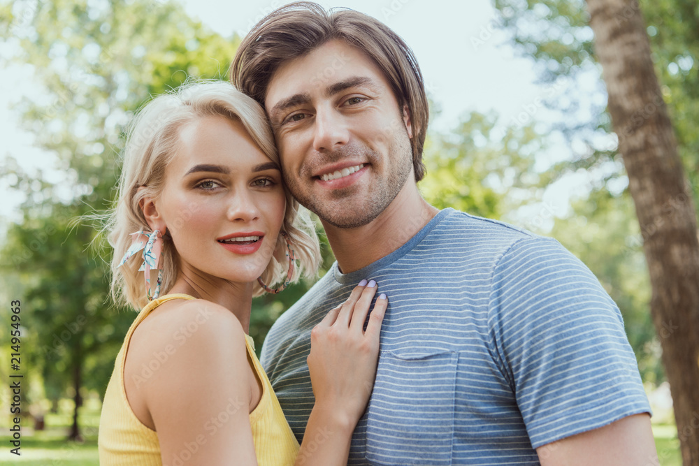 smiling couple hugging and looking at camera in park