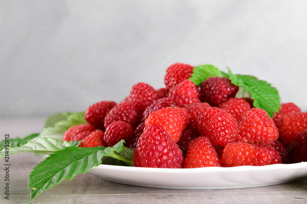 Red fresh raspberries on white rustic wood background. Plate with natural ripe organic berries with green leaves.flat lay with copy space Red fresh raspberries on white rustic wood background. Plate with natural ripe organic berries with green leaves.flat lay with copy space