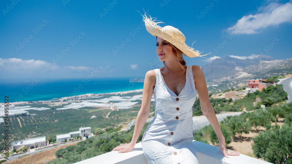 Young woman in white dress and hat is posing on olive garden and sea coast background, Falassandra region, Crete, Greece