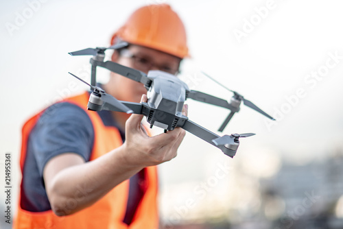 Young Asian engineer holding drone at construction site. Using unmanned aerial vehicle (UAV) for land and building site survey in civil engineering project.