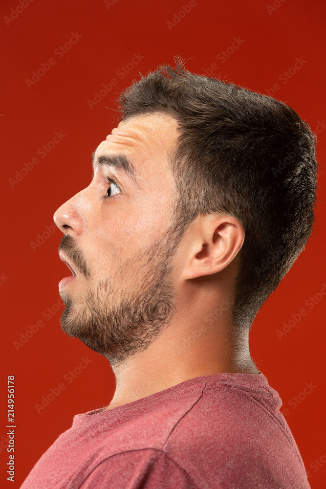 Fototapeta premium The young attractive man looking suprised isolated on red