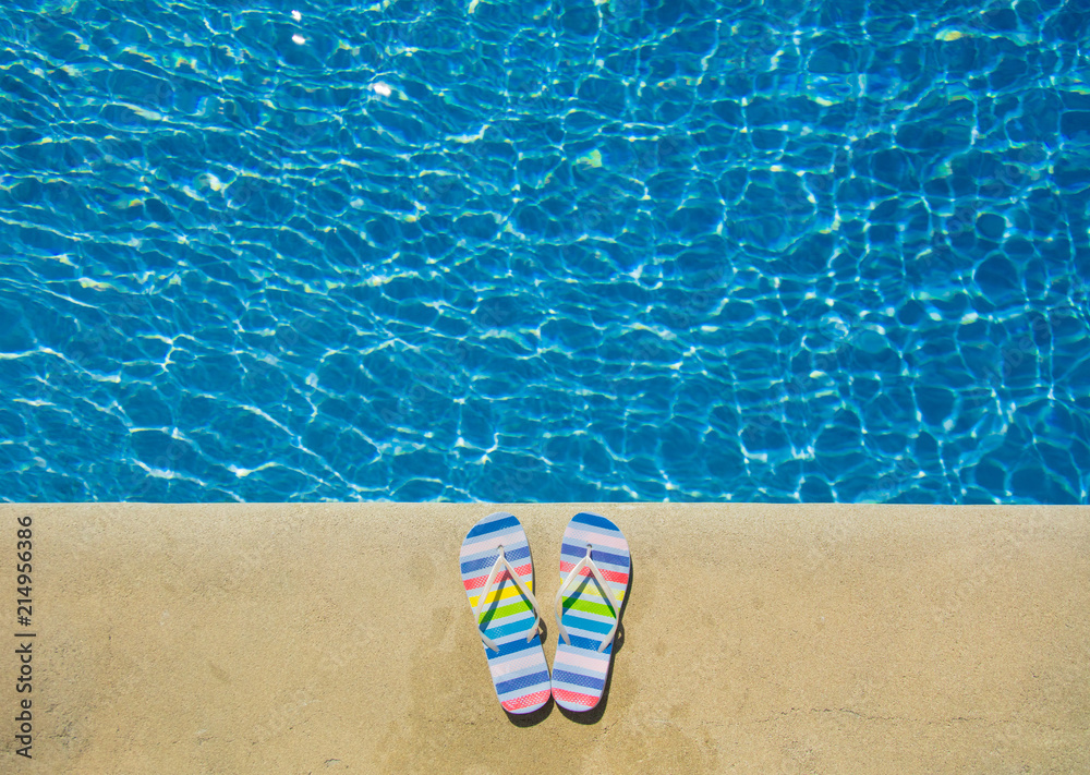 Naklejka premium Colored summer sandals near blue pool. Above view