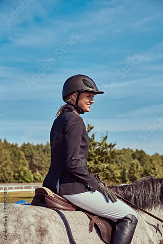Portrait of a smiling female jockey on dapple gray horse in the open arena.