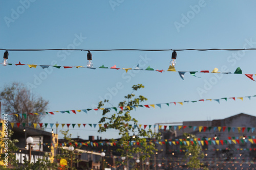 Multicolored flags against the background of the blue sky and Open Air Festival. ribbon with flags of red, yellow, violet, orange and blue colors. Colorful flags on rope hanging outside for holiday