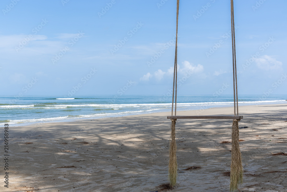 Wooden swing hanging under the tree on the beach with blue sky. Wooden swing hanging under the tree on the beach with blue sky.
