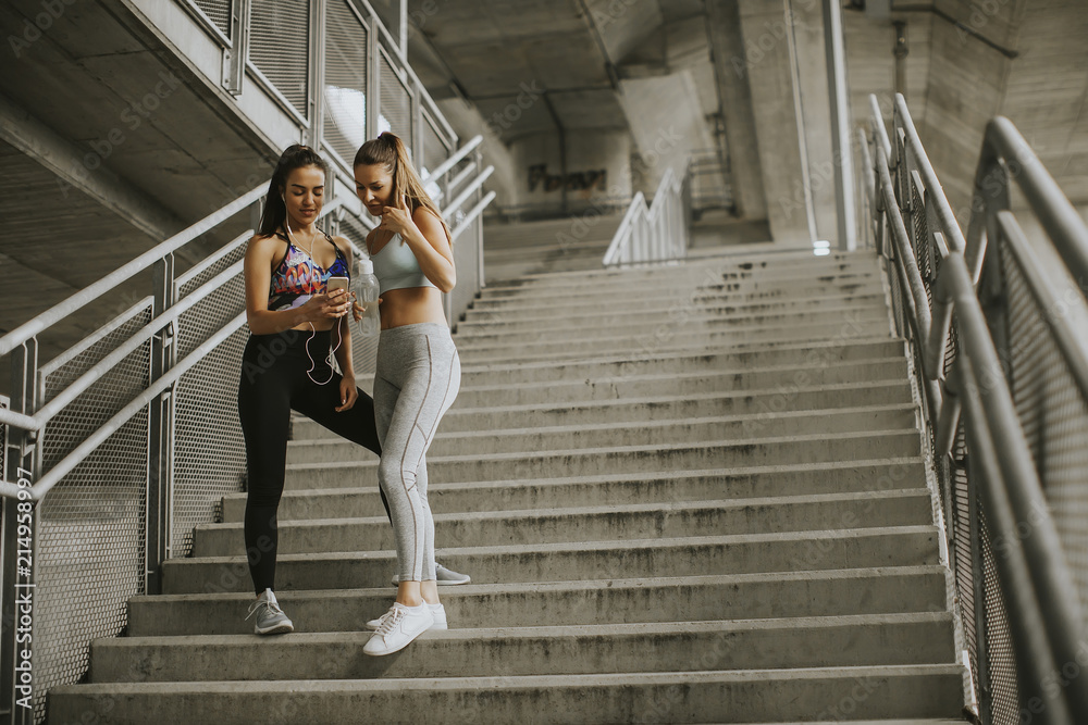 Two female runners looking on smart phone an rest after jogging Two female runners looking on smart phone an rest after jogging