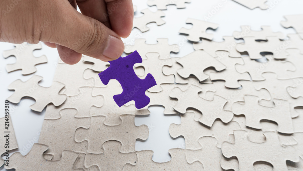 Fototapeta premium Hand put missing jigsaw puzzle into the paper board