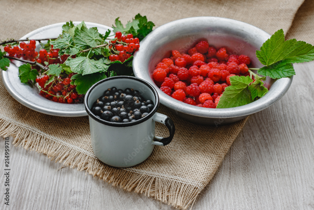 Rustic still life of ripe red and black currants, raspberries with leaves in a rustic plate and mug on the background of sacks, healthy food and vitamins. Mixed summer berries. Rustic still life of ripe red and black currants, raspberries with leaves in a rustic plate and mug on the background of sacks, healthy food and vitamins. Mixed summer berries.