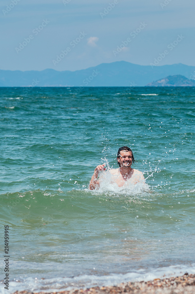 Handsome man having fun in the sea, splashing water around, cute smile. Summer holiday concept