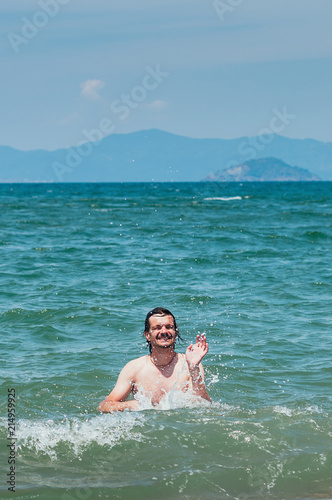 Handsome man having fun in the sea, splashing water around, cute smile. Summer holiday concept © Kalinova Olena