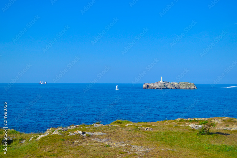 Lighthouse in the middle of an island on the sea, with boats navigating around. Cantabria, Spain