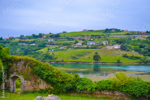 View of green fields in front of Brazo Mayor river, in San Vicente de la Barquera, Cantabria, Spain, with houses at the background