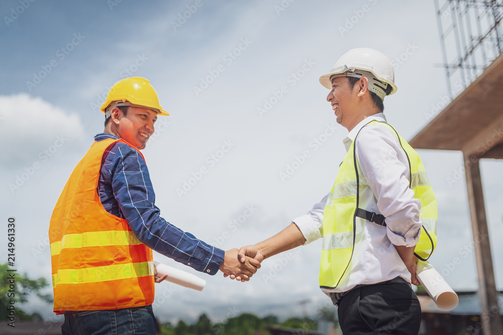 Handsome construction workers in protective helmets and vests are shaking hands while working in the office center, Horizontal, Blurred background Handsome construction workers in protective helmets and vests are shaking hands while working in the office center, Horizontal, Blurred background