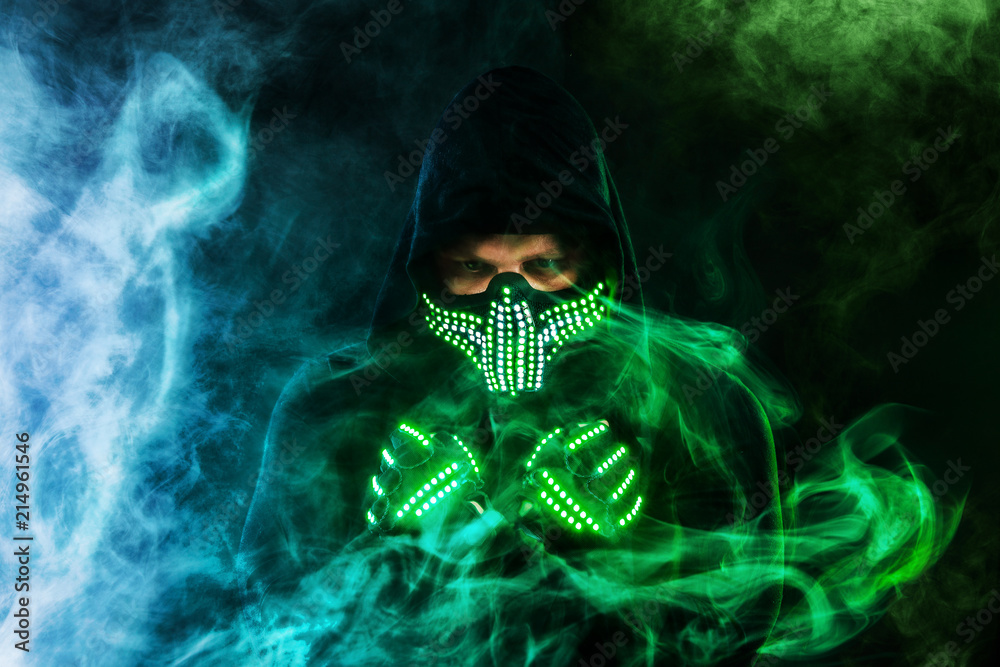 Mysterious man in black wear, neon mask and gloves. Character pastor or  wizard in robe from the future. Assassin with strong face expression.  Fantasy book or computer game cover concept. Stock Photo