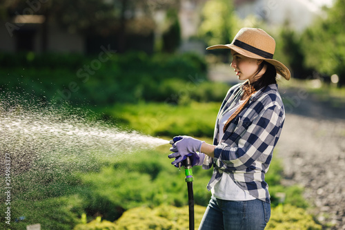 Beautiful young gardener woman watering garden in hot summer day