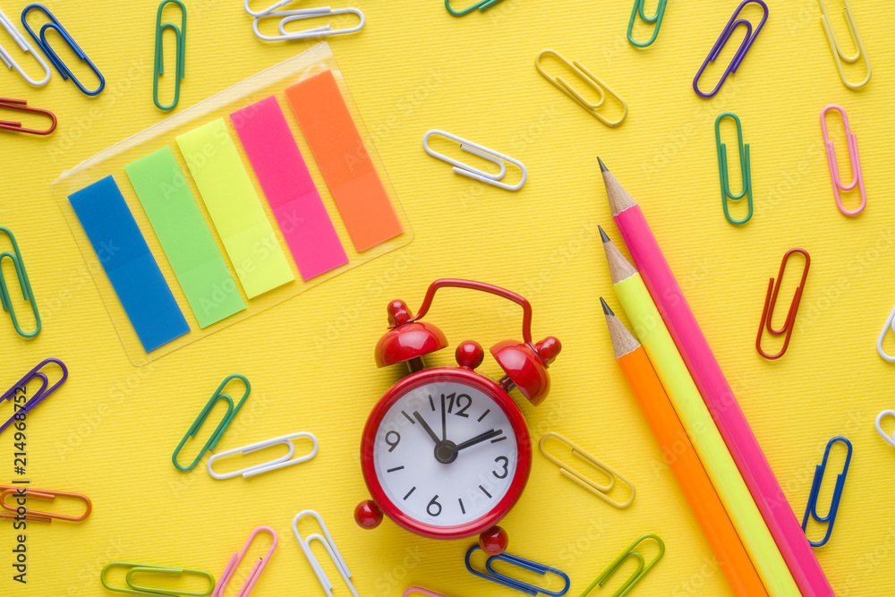 Pencils and colored paper clips, clock alarm on yellow background. Copy space Pencils and colored paper clips, clock alarm on yellow background. Copy space