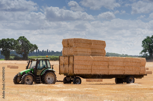 green tractor in field during harvest collecting bales of hay on a trailer photo