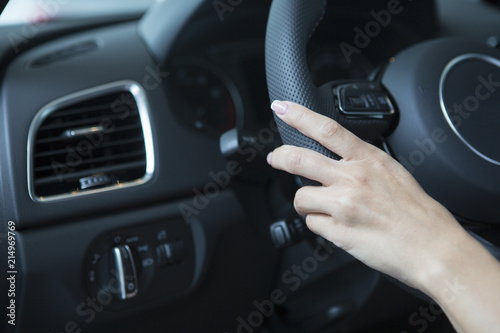 The hand of a girl with a stylish manicure lies on the handlebars in a saloon car. © biggur