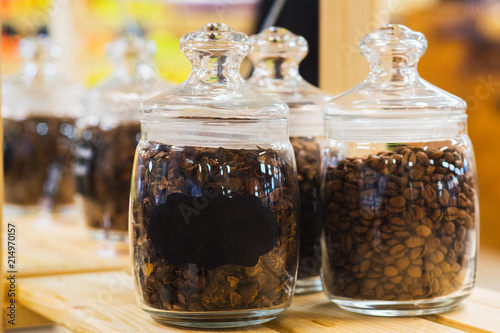 Traditional black coffee beans in a glass jar on the counter of a small market or store. 