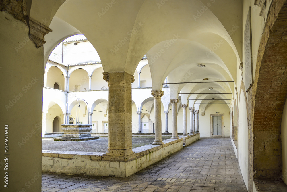 Ancient Franciscan cloister with columns and capitals in Corinthian style. At the center is the well
