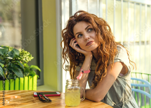 Attractive curly hair woman enjoying good day, sitting at the cafe and dreming. Looking aside. photo