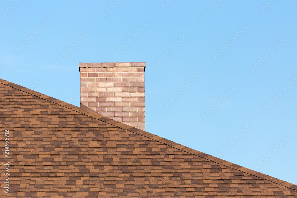 Red brick chimney on shingle roof od new modern house under blue sky on sunny day in summer