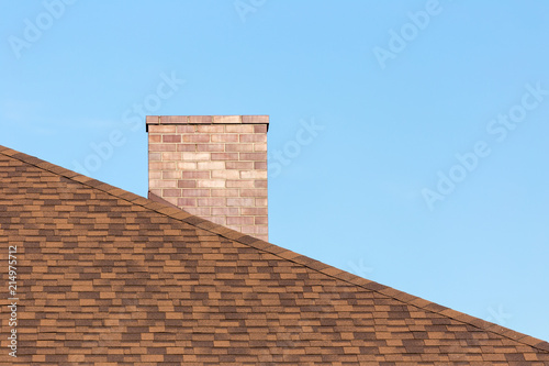 Obraz na plátne Red brick chimney on shingle roof od new modern house under blue sky on sunny da