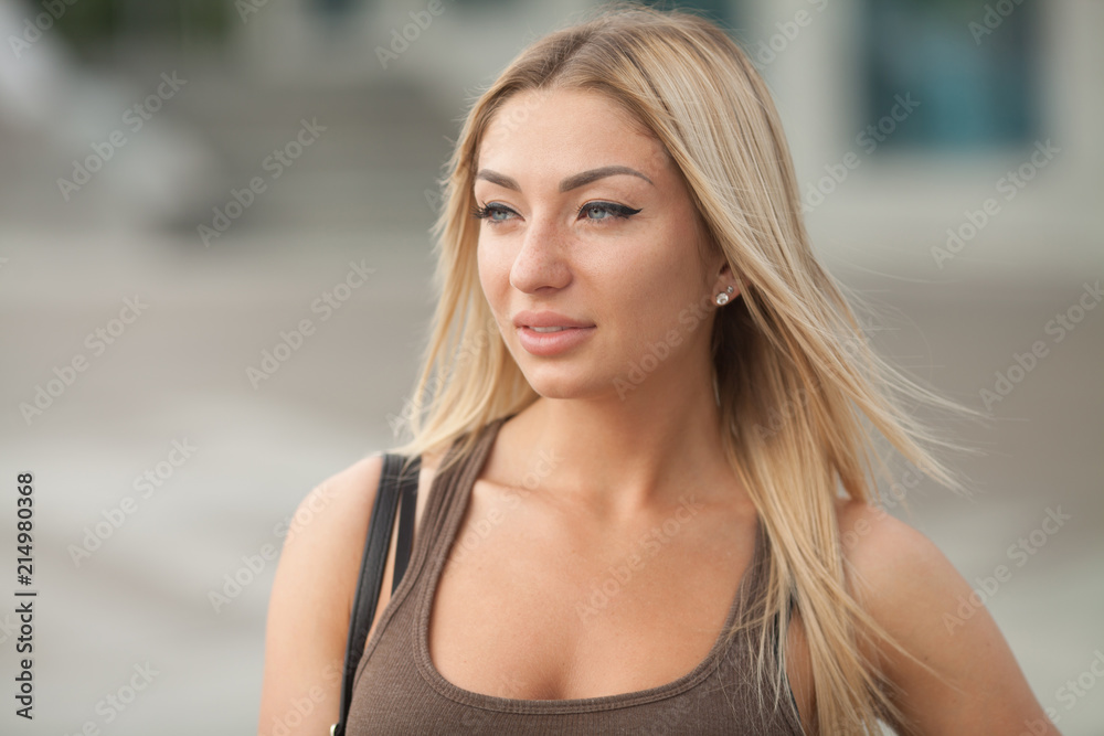 Fototapeta premium A portrait of a beautiful blonde young Caucasian woman outdoor. Young smiling woman outdoors portrait. Soft sunny colors.Close portrait.