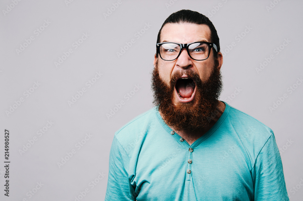 Obraz premium Young bearded man yelling and looking at the camera on white background.