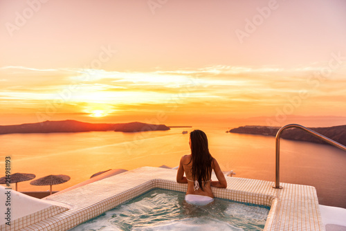 Luxury travel Santorini vacation woman swimming in hotel jacuzzi pool watching sunset. Europe resort destination holiday for honeymoon getaway.