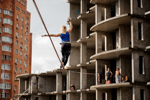 Rear view woman walking on the slackline rope to the unfinished buildings