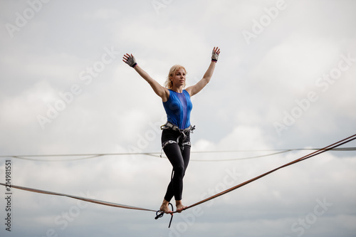 Young smiling woman standing with arms raised on the slackline rope