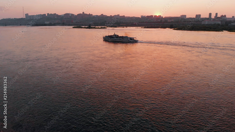Aerial view of the ship sailing on the river in the city at sunset.